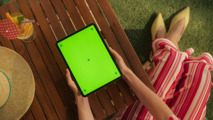 匿名女性在花园中使用带有模拟绿屏Chromakey显示屏的数字平板电脑的俯视图。一名女子一边放松一边