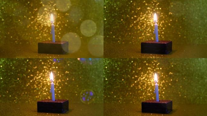 一支燃烧的蜡烛在小小的生日蛋糕上，金色闪闪的背景和串灯闪耀
