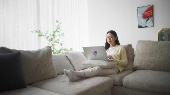 年轻美丽的亚洲女性浏览互联网，使用笔记本电脑在家里，计划一个令人兴奋的旅行行程，她的度假之旅，而坐在