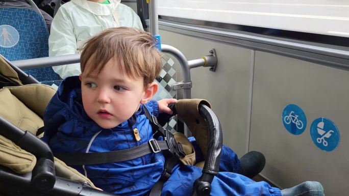 The child is sitting in a stroller on the bus, wit