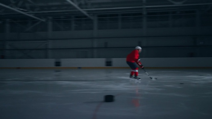 一名身穿红色球衣的冰球运动员在冰上训练的高强度镜头，他快速移动并向守门员进球