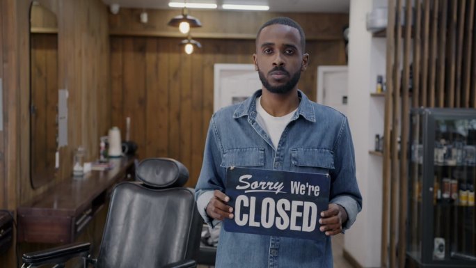 慢动作的年轻非洲裔美国人的肖像拿着对不起，我们是关闭的标志在理发店