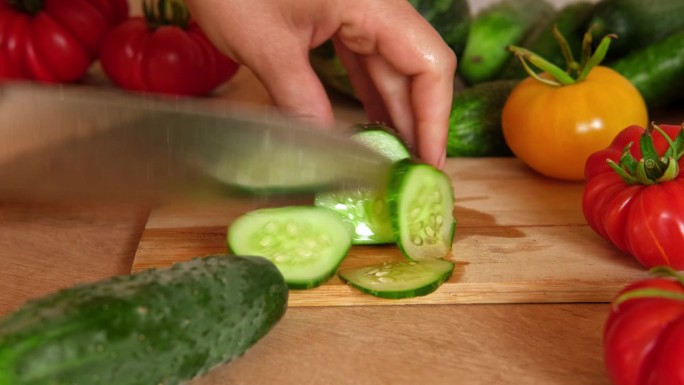 一个女人正在用刀切新鲜的生蔬菜。西红柿、黄瓜在木板上切成片。在家里做一顿健康的素食餐。准备素菜的切食