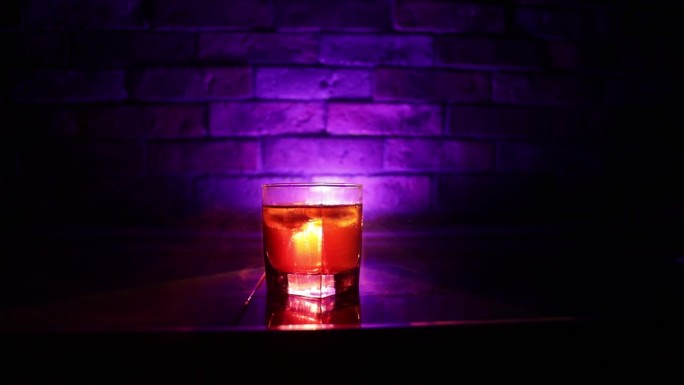 威士忌饮品概念。一杯威士忌和冰与颜色光和雾在黑暗的酒吧背景。有选择性的重点