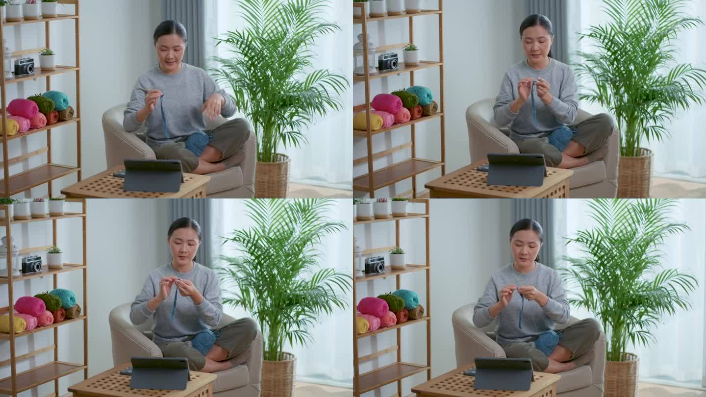 亚洲妇女教如何钩针编织在线视频剪辑在平板电脑坐在家里的客厅。