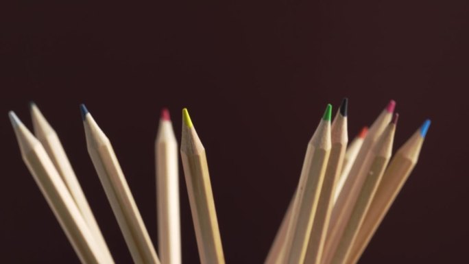 收集不同的彩色学校铅笔用于绘画和着色。一套彩色铅笔旋转在一个棕色的背景，宏观。回到学校的概念。彩虹铅
