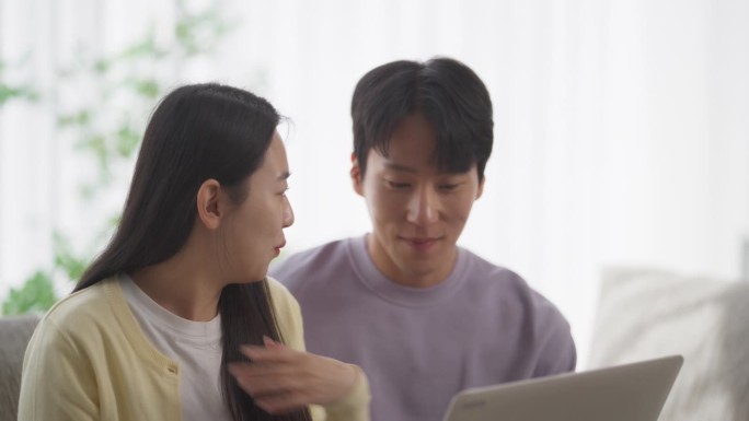 一对幸福的韩国夫妇在家里度过美好时光，在舒适的公寓里营造和谐的氛围，在笔记本电脑上观看韩剧