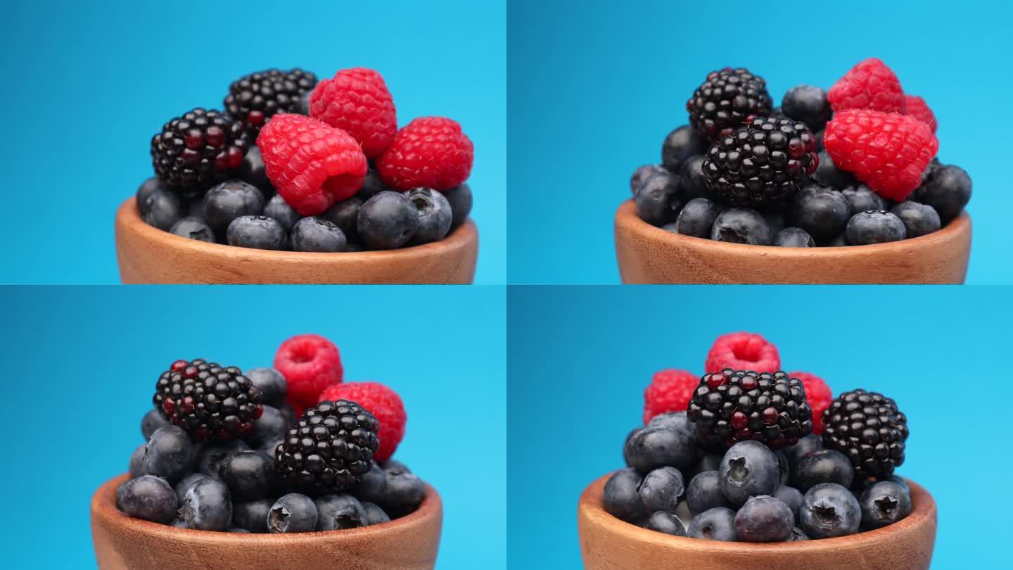 把新鲜的野莓放在碗里，转一圈。成熟的蓝莓，覆盆子，黑莓以蓝色为背景