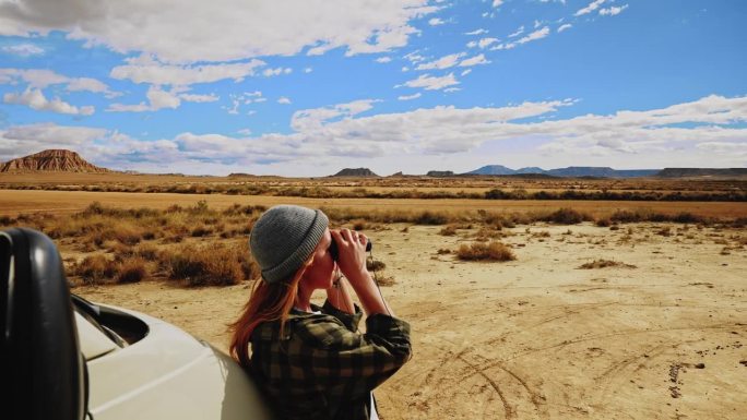 一名女子在穿越摩洛哥的公路旅行中休息时，用双筒望远镜观察沙漠