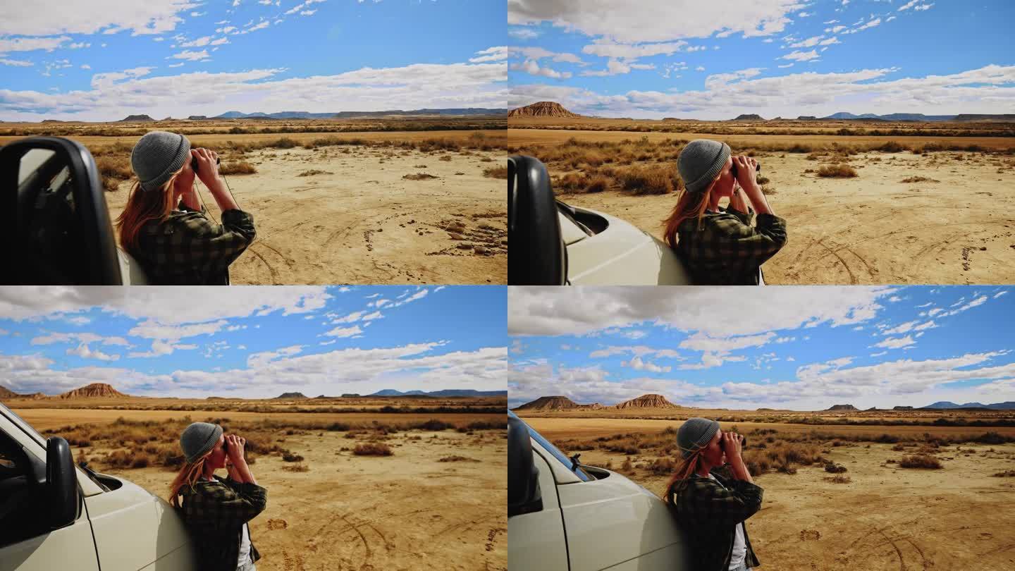一名女子在穿越摩洛哥的公路旅行中休息时，用双筒望远镜观察沙漠