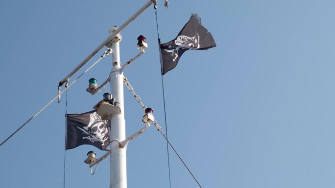 Jolly Roger或海盗船的旗帜挥舞着旗杆和蓝天，骷髅和交叉的骨头，加勒比海盗和黑珍珠。扯掉眼泪