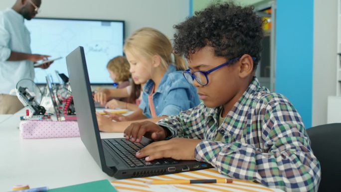 黑人男孩在儿童科技俱乐部为电动机器人编写计算机程序
