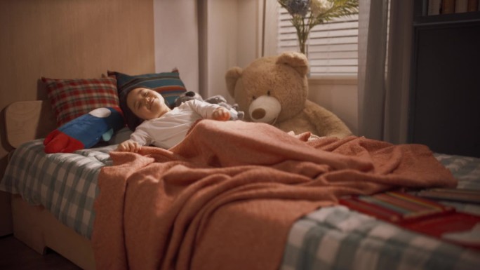 一个可爱快乐的韩国女孩在她可爱的房间里小睡后醒来的肖像。小孩坐在床上，抱着毛绒玩具，伸展双臂，可爱地
