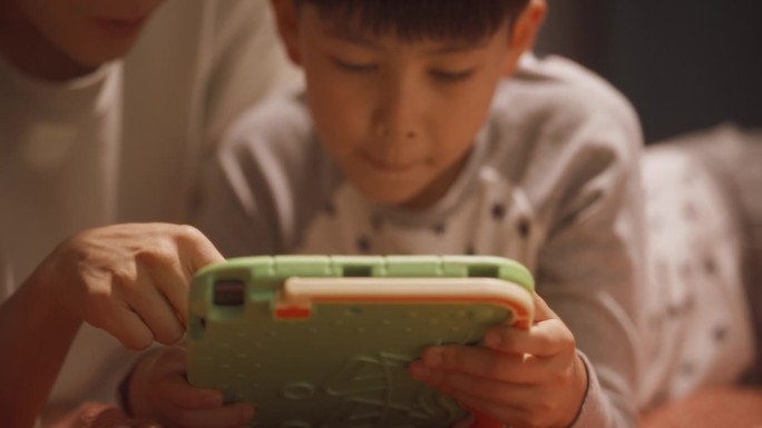 一位父亲和他可爱的小儿子在家里使用平板电脑的照片。年轻的韩国男子看着他的孩子在教育学习游戏中获胜