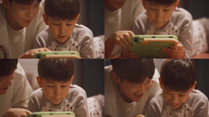一位父亲和他可爱的小儿子在家里使用平板电脑的照片。年轻的韩国男子看着他的孩子在教育学习游戏中获胜