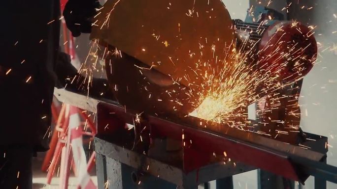 工人在生产车间用圆锯切割金属通道，火花飞溅。