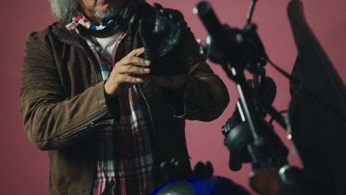 一个老摩托车手穿着皮夹克，戴着手套，坐在他时髦的摩托车上。