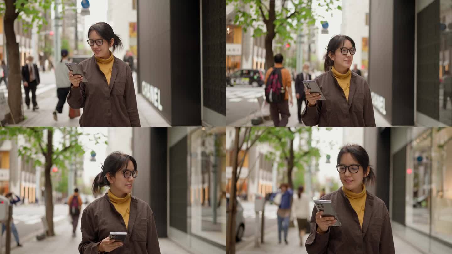 年轻的亚洲女人走在街上看智能手机。