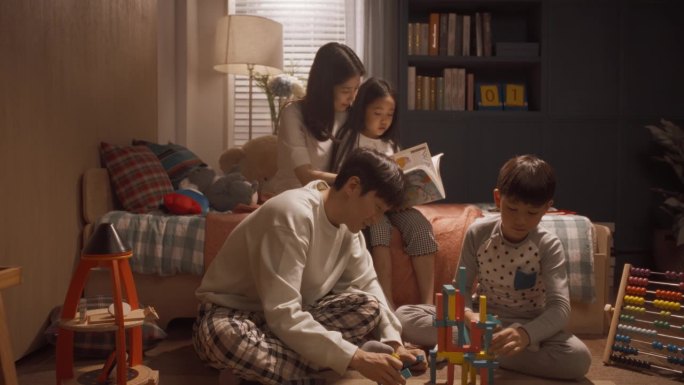 一个美丽的亚洲家庭的肖像摆姿势，微笑，看着相机。快乐的韩国父母在家里和两个孩子玩耍，弟弟和妹妹忙着读