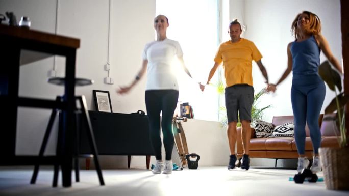 SLO MO Fit年轻朋友一起做开合跳，在阳光明媚的客厅享受家庭锻炼。活力，运动，锻炼，健康的生活