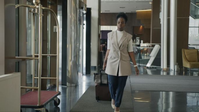 多莉拍摄的非裔美国女商人带着行李走在酒店大堂