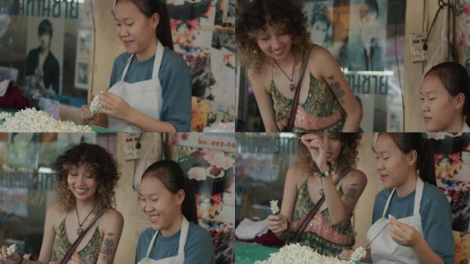 在泰国曼谷，一位兴高采烈的女游客向泰国花店老板请教如何制作花环。
