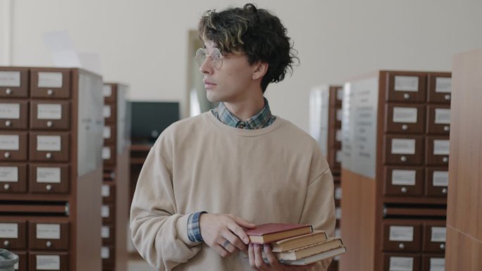 多莉拍摄了一个聪明的年轻人走在现代图书馆里，拿着书看着书架和人的肖像