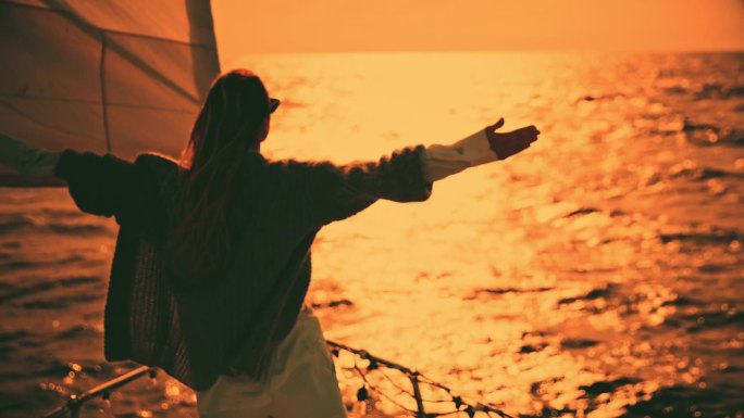 帆船上的一个女人伸开双臂欣赏日落。无忧无虑的女人在夕阳下张开双臂欣赏大海