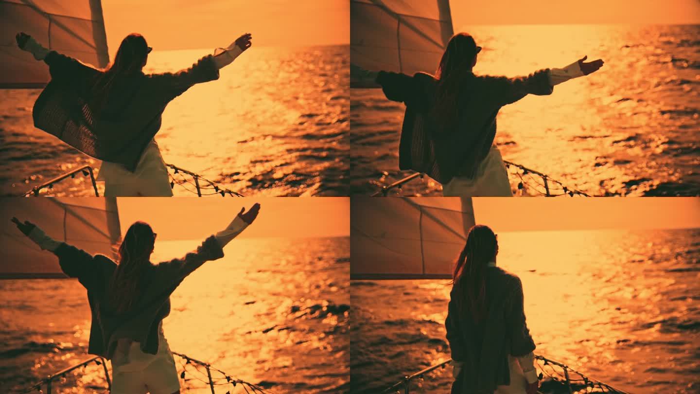 帆船上的一个女人伸开双臂欣赏日落。无忧无虑的女人在夕阳下张开双臂欣赏大海