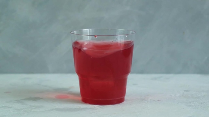 红色清爽饮料在塑料杯灰色背景。水果冰茶。五彩缤纷的夏日无酒精清凉饮料加冰块。视频，慢动作