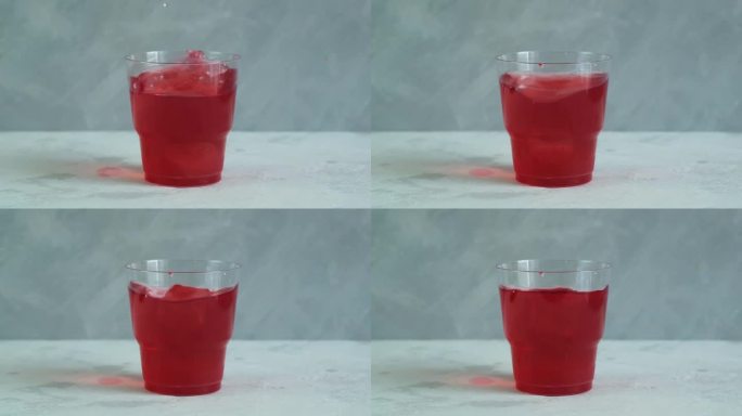 红色清爽饮料在塑料杯灰色背景。水果冰茶。五彩缤纷的夏日无酒精清凉饮料加冰块。视频，慢动作