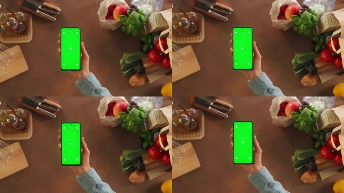 顶部静态视图匿名妇女使用智能手机与模拟绿色屏幕Chromakey显示厨房桌子上的器具和食物配料。观看