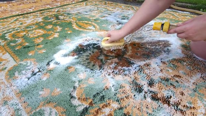 在院子里用带清洁剂的刷子洗地毯