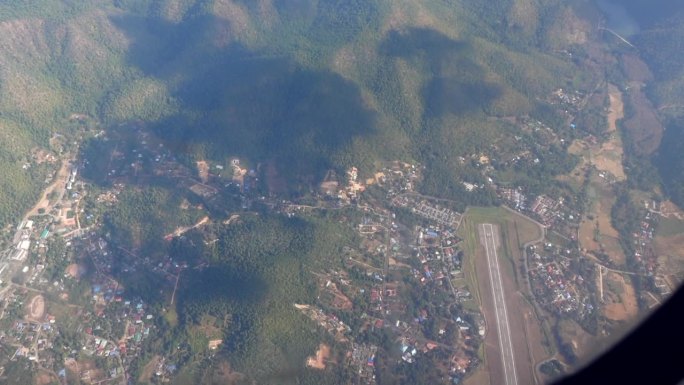 俯览泰国小机场跑道和当地小镇山地上空的飞机窗景