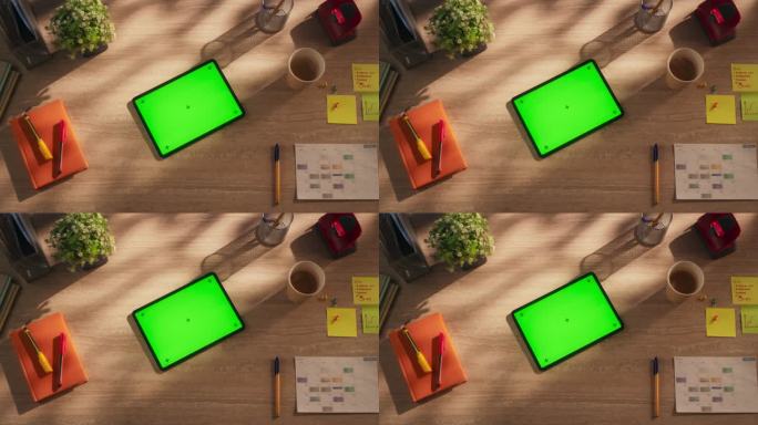 平板电脑的顶部向下静态视图与模拟绿屏显示。一个设备水平躺在一个创意办公室的木桌上。在线数字营销活动模