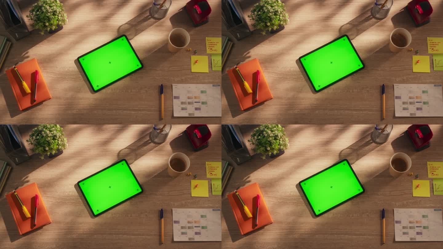 平板电脑的顶部向下静态视图与模拟绿屏显示。一个设备水平躺在一个创意办公室的木桌上。在线数字营销活动模