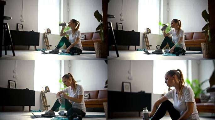 专注的，健康的年轻女子在客厅地板上从水瓶里喝水，在家庭锻炼后休息。运动，健身，健康的生活方式，积极的