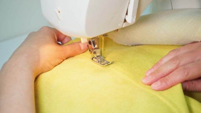 女裁缝在黄色布料上缝缝。对现代缝纫机的缝纫过程进行近距离观察