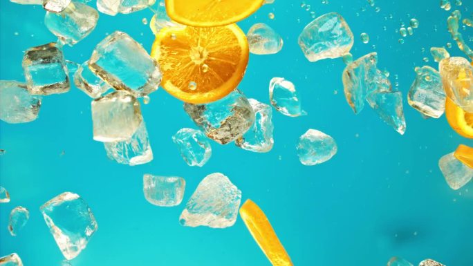 多汁的甜橙和飞冰块或水飞溅或倒滴果汁在1000 fps超级慢动作。橘子片和冰块在蓝色背景下掉落或爆炸