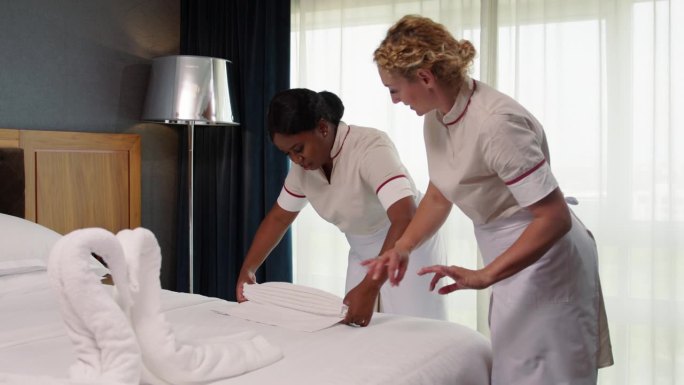 两个穿制服的女仆在一起装饰酒店的床铺
