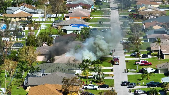 从上面看着火的私人房屋，消防员正在扑灭被飓风伊恩风损坏的屋顶因短路而引燃的火焰。佛罗里达郊区发生家庭