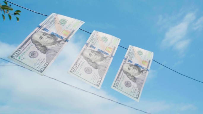 在蓝天的背景下，在晒衣绳上晒着一百美元的钞票