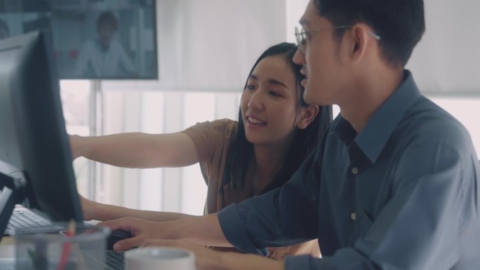在一个现代化的办公空间里，亚洲商人男女正在电脑前工作并与同事讨论。