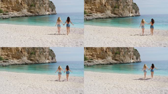 两个迷人的年轻女子跑向大海在热带海滩暑假兴奋地享受清凉的清澈的蓝色的水游泳穿着牛仔短裤