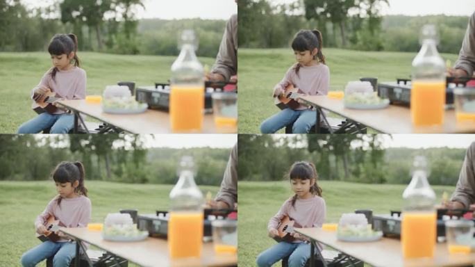 快乐的小女孩在度假时与家人在绿地野餐时玩尤克里里，唱着喜欢的音乐。