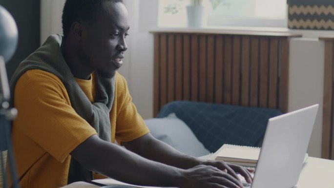 年轻的非裔美国学生，在家用笔记本电脑打字，忙着完成大学作业