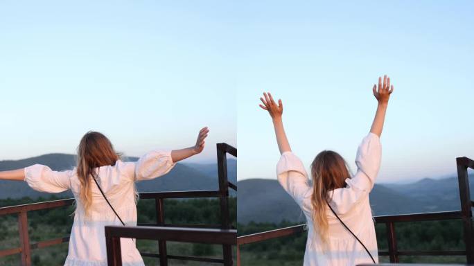 美丽快乐的金发女孩，蓬松的头发，穿着白色的裙子，举起她的手，在日落的群山中快乐。垂直视频。