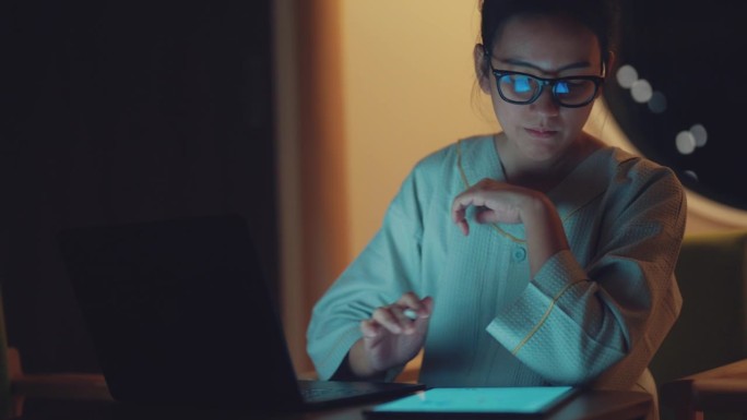 亚洲年轻女性在数码平板电脑上写作，在晚上带着严肃的情绪工作。
