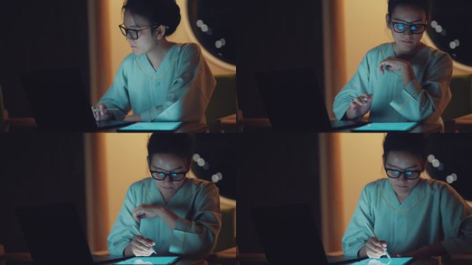 亚洲年轻女性在数码平板电脑上写作，在晚上带着严肃的情绪工作。