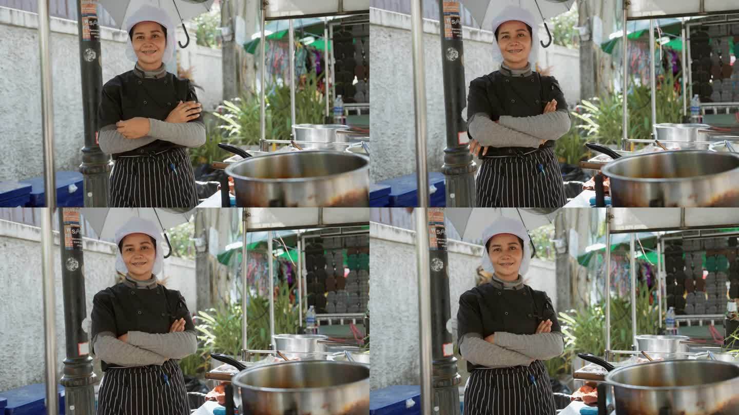 泰国一位面带微笑的街头小吃店老板抱着双臂，为自己的小生意感到自豪。